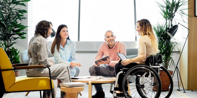 Two women and a man talking to a woman in a wheel chair holding a tablet computer